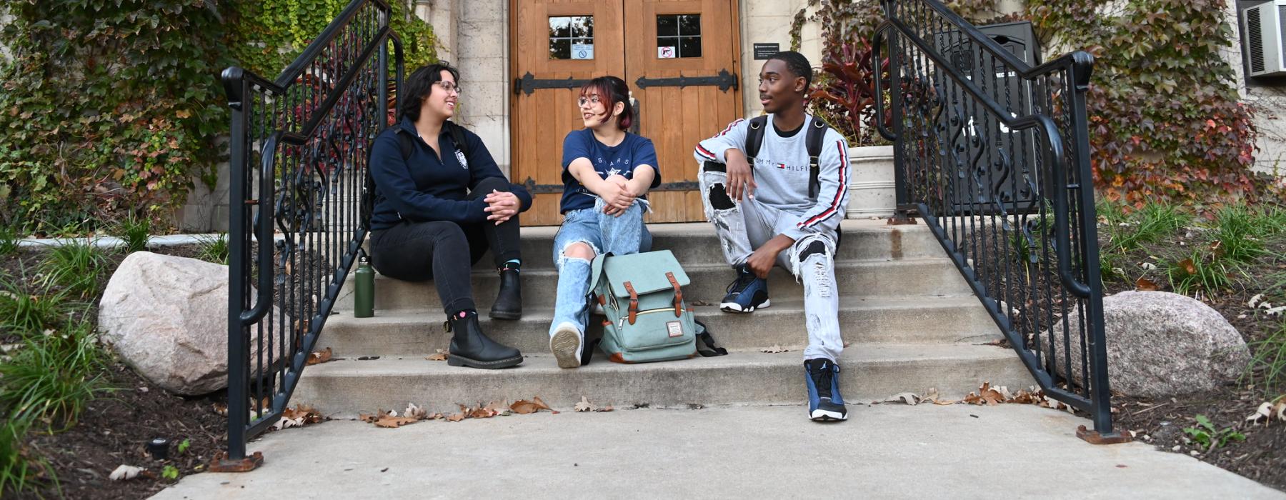 Three students sitting on the front steps outside Lewis Hall