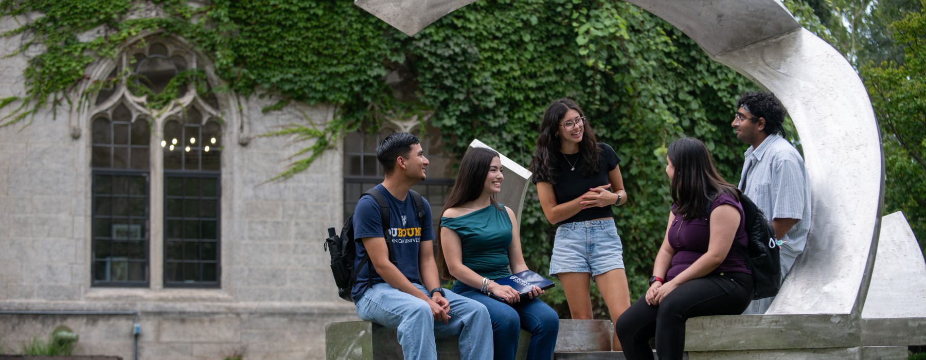 A group of Dominican University students sit and chat around a sculpture on campus.