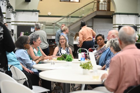A group of older white and Black women and men sit at tables talking during Dominican University's Alumni Weekend.