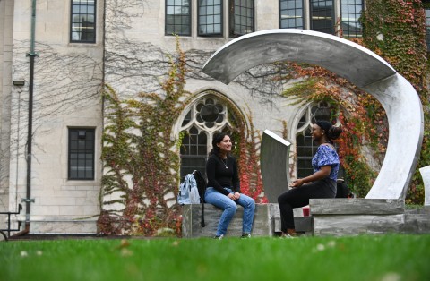 Two female students seated at the sculpture