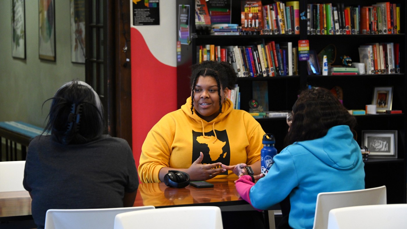 Three students at a desk with books in background