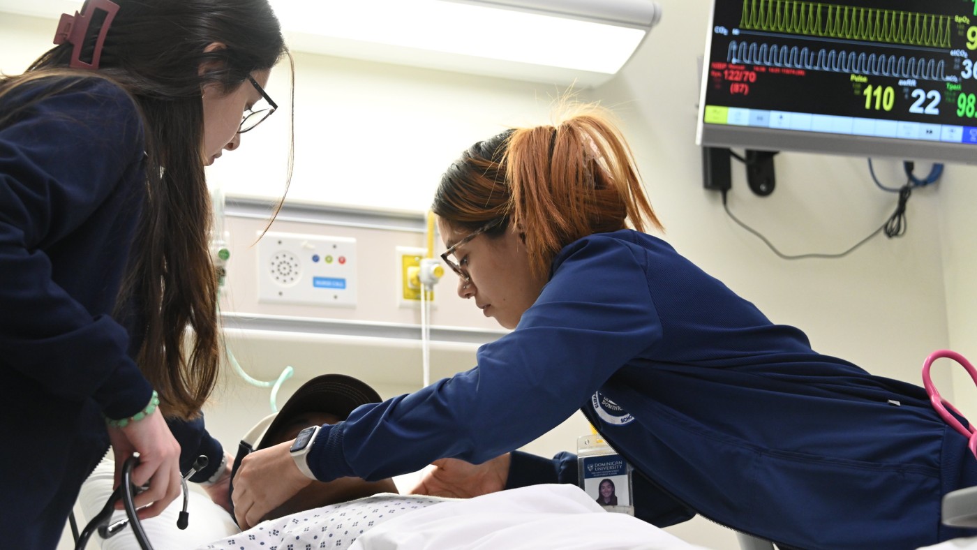 Two female nursing students work on a patient simulator manikin in a hospital bed in Dominican's simulation lab.
