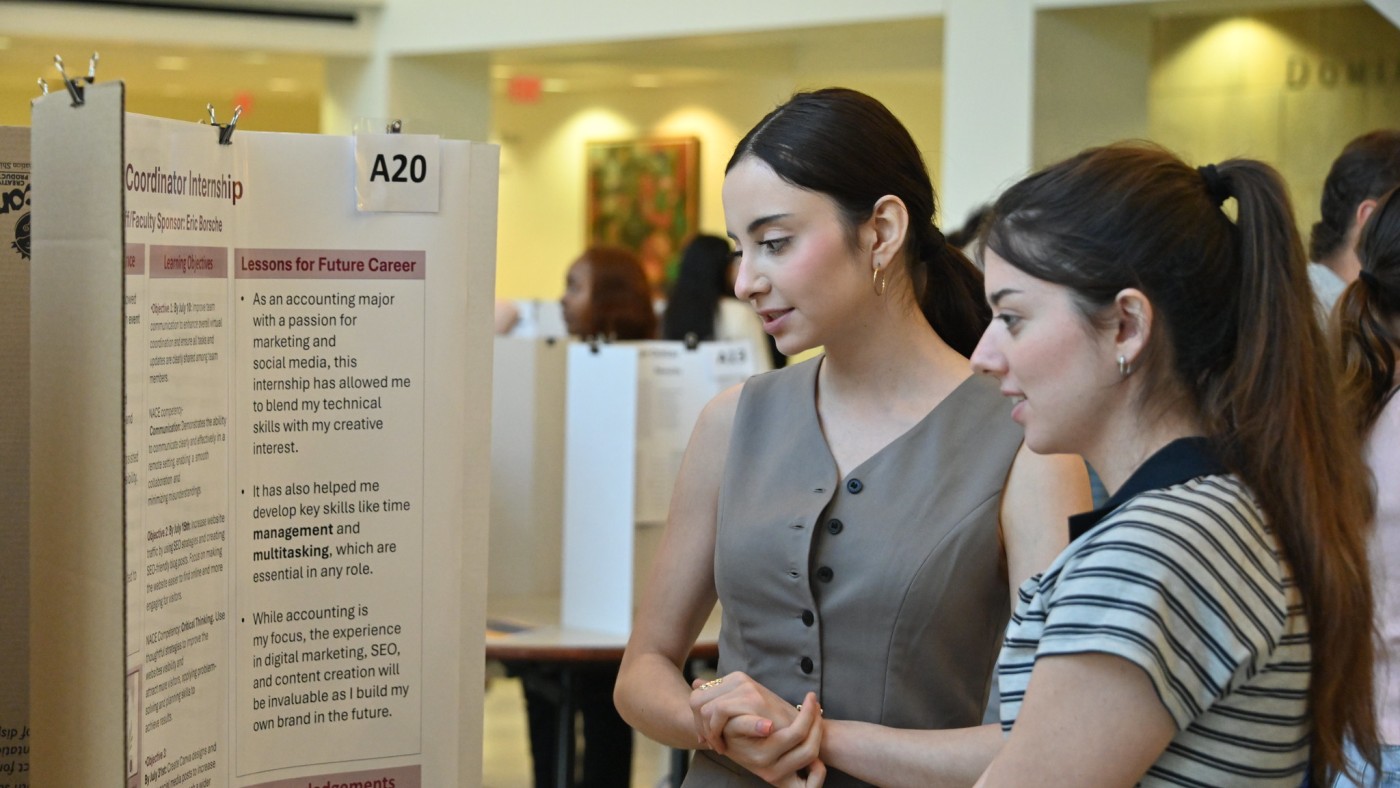Two female students in front of poster board exhibit