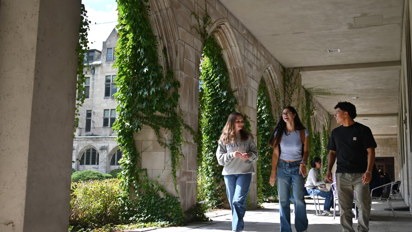 Students walk across Dominican University's lower Cloister Walk, which is covered in green ivy.