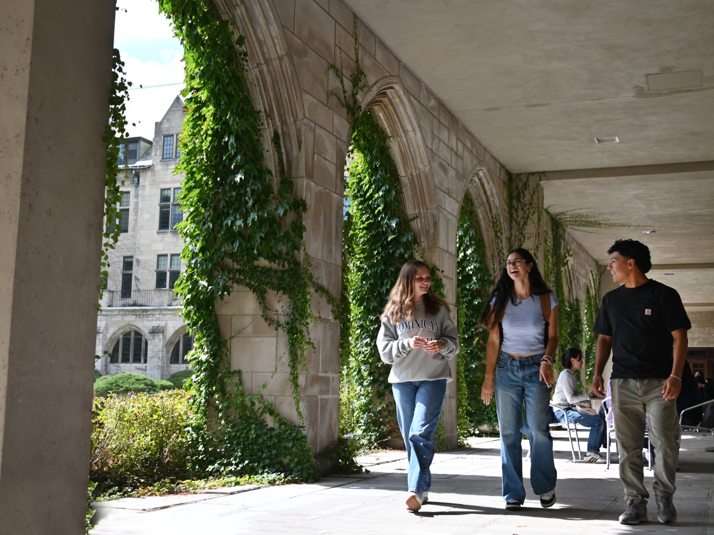 Students walk across Dominican University's lower Cloister Walk, which is covered in green ivy.