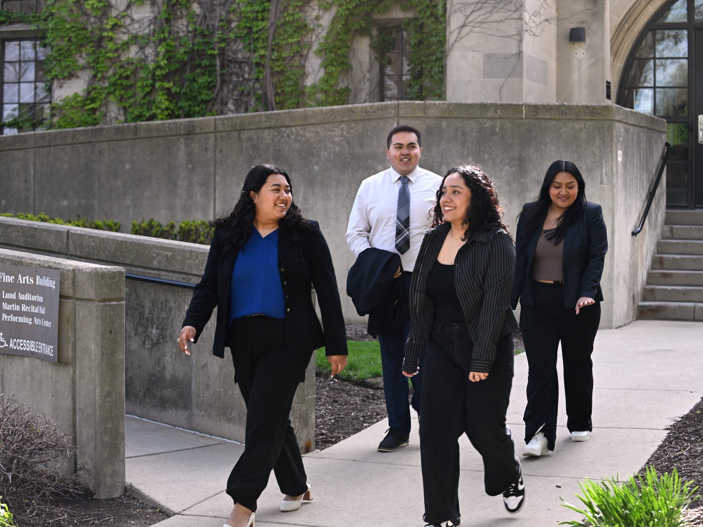 Four professionally dressed students leaviong the FA Building